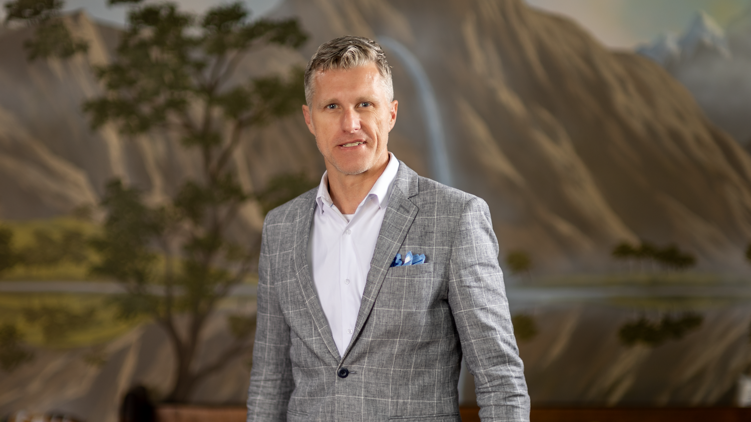 Jim Slaton, founder of Want Web Design, standing in front of a mountain landscape mural
